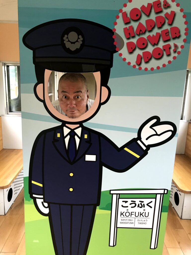 幸福駅の車掌イラスト顔出しパネルで記念撮影する男性