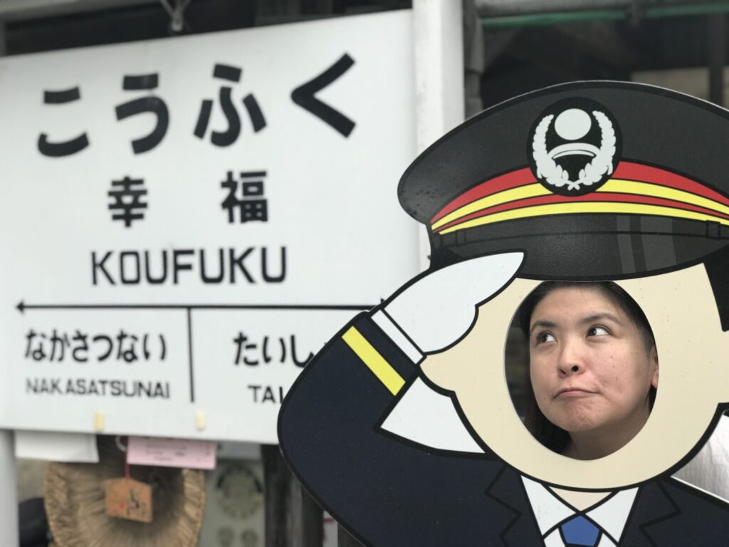 幸福駅の看板前で駅長の顔出しパネルを楽しむ女性
