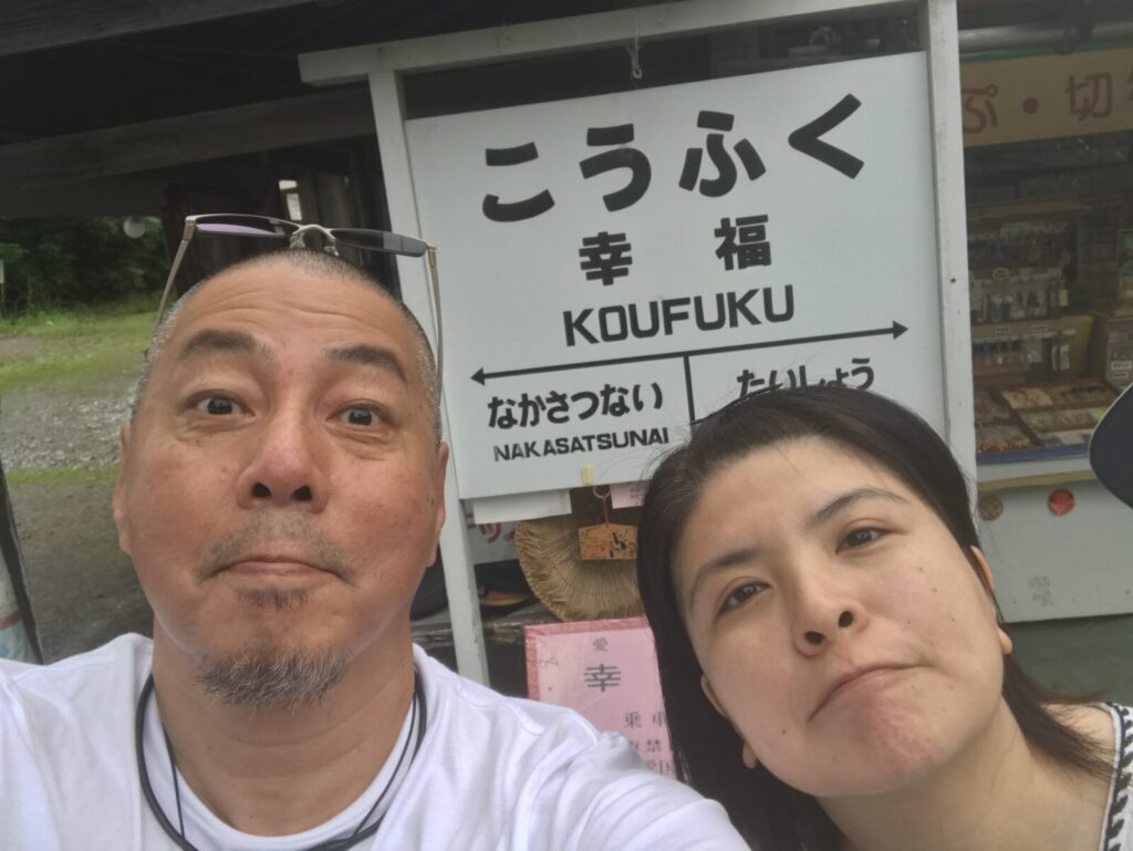幸福駅の看板前でセルフィーを撮る夫婦