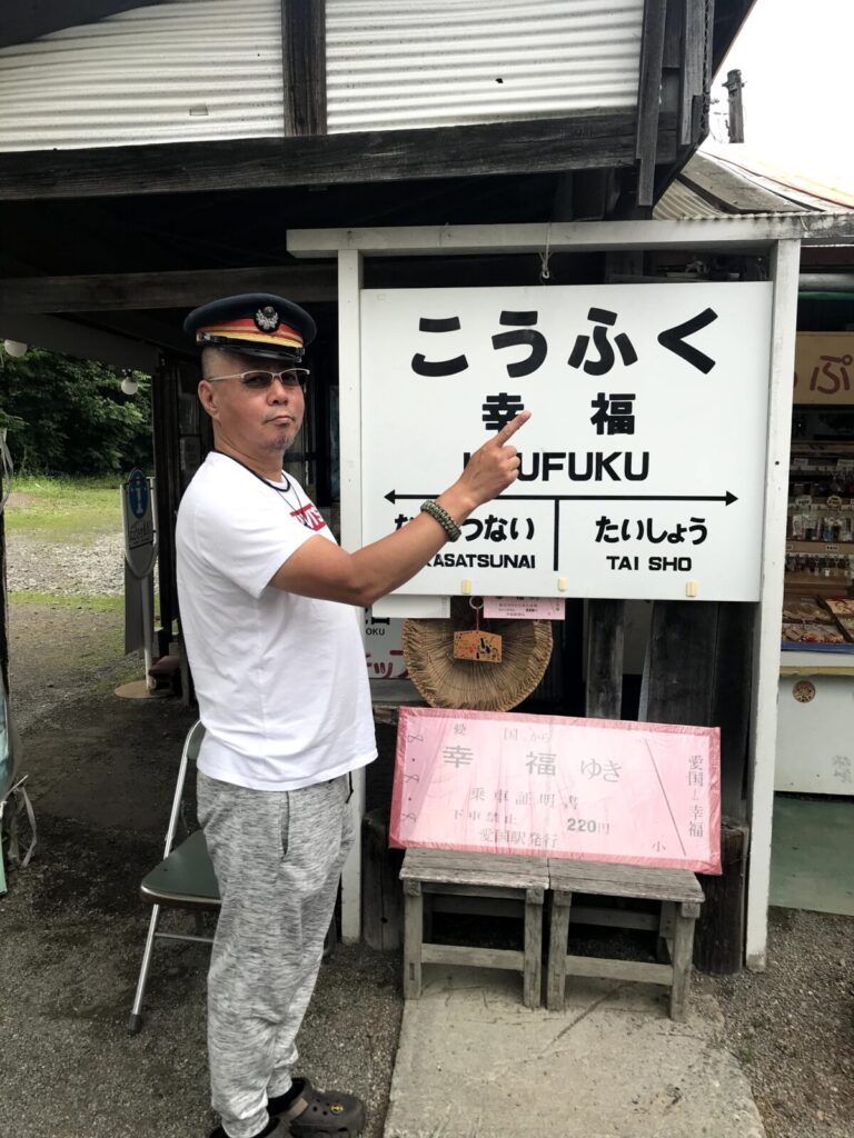 幸福駅の駅名標の前で指をさしながら記念撮影をする男性