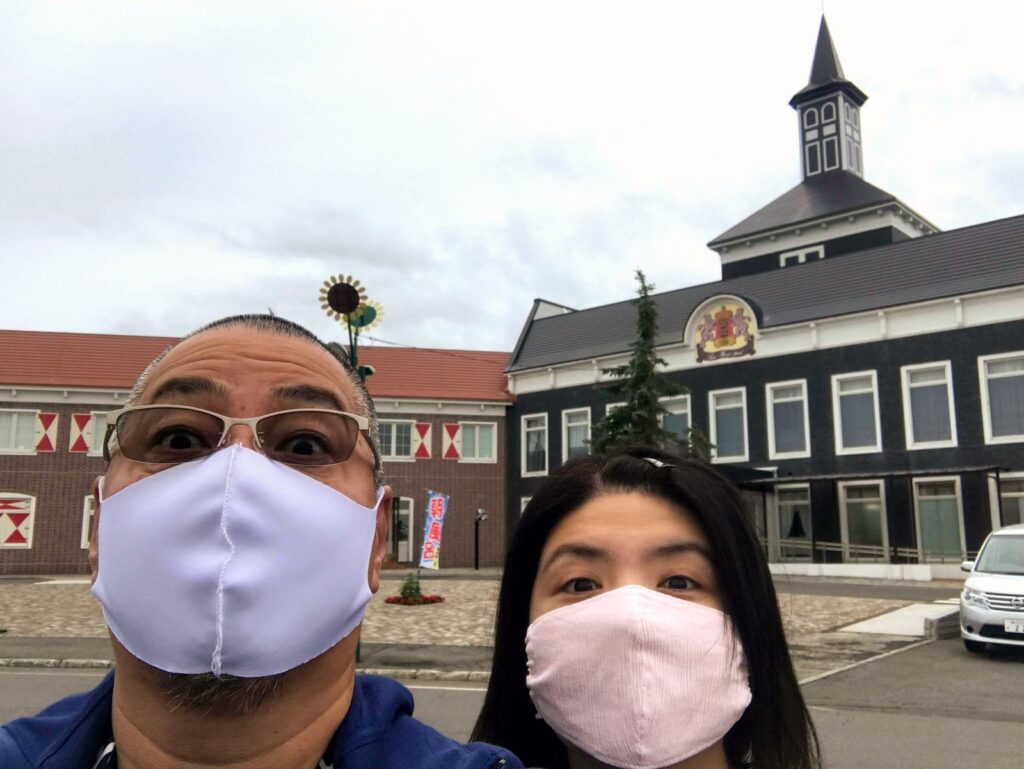 道の駅サンフラワー北竜の建物の前で撮った、マスク姿のくま嫁と旦那の自撮り