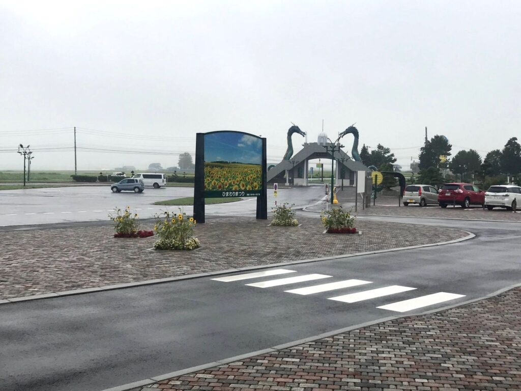 雨にぬれた道の駅サンフラワー北竜の駐車場と、ひまわりまつりの看板、竜の門