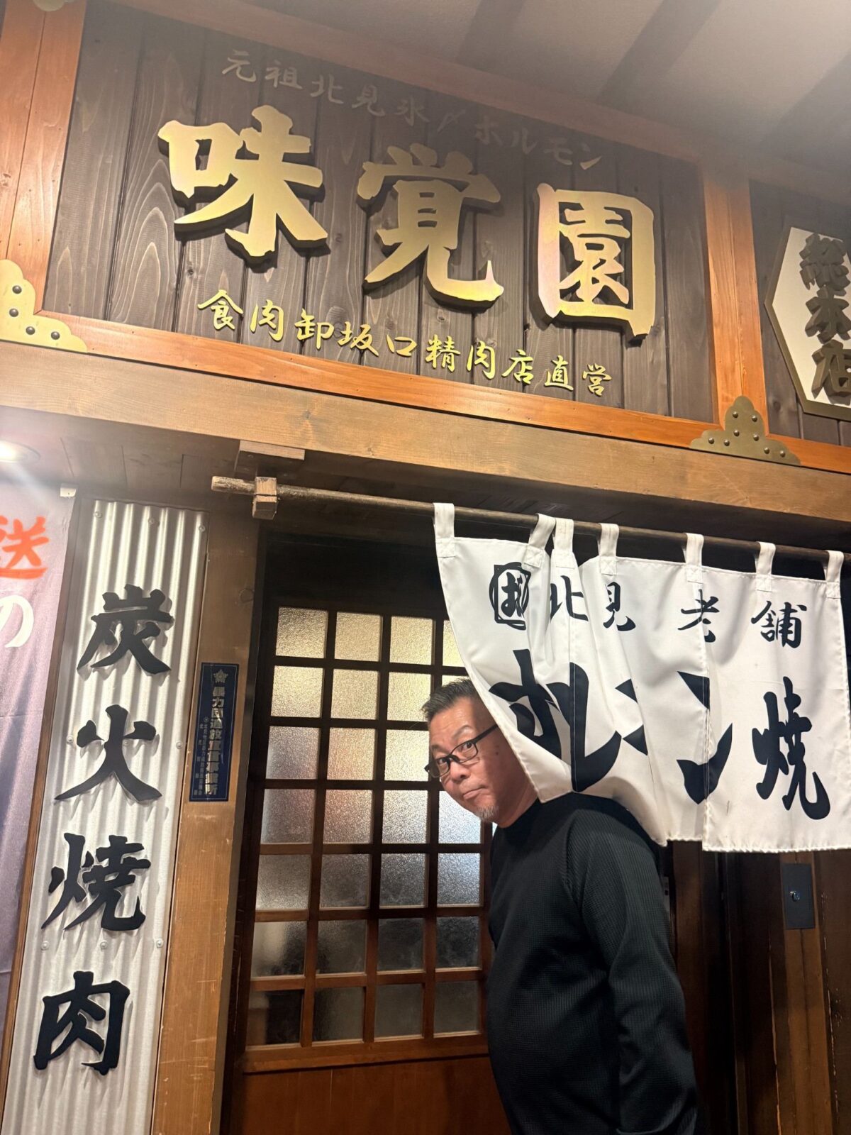 木の看板とのれんがある味覚園 総本店の入口と手前に立つ人物