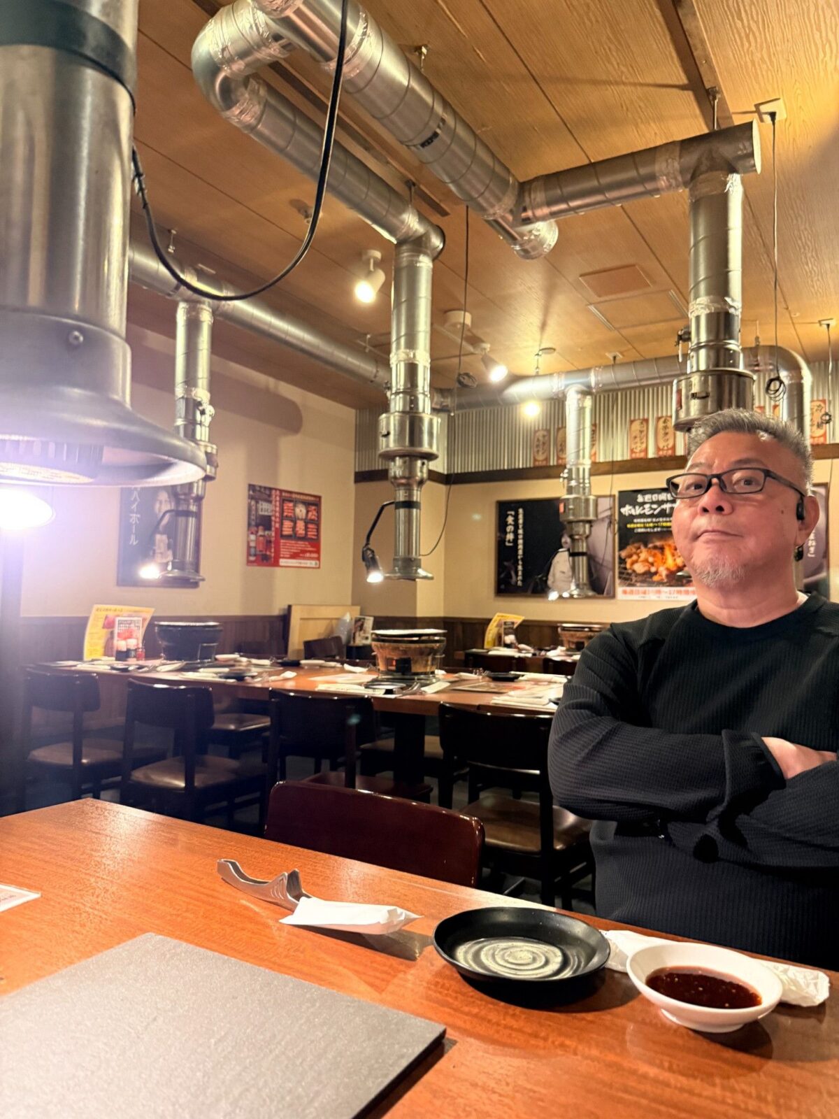 木のテーブルと排煙ダクトが並び、人物が座っている焼肉店内