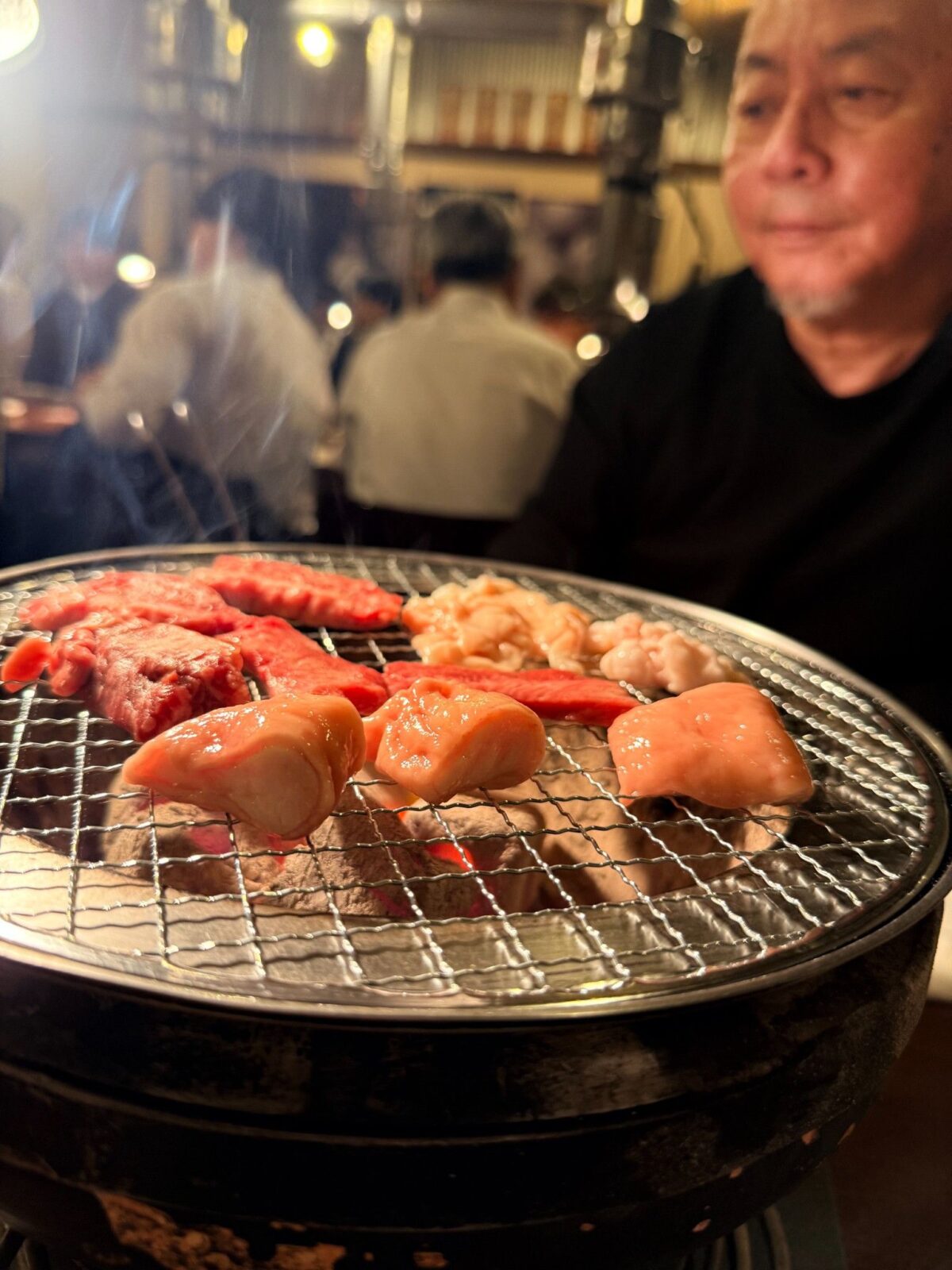 炭火の網に並んだ肉とホルモン、背景に写る人物