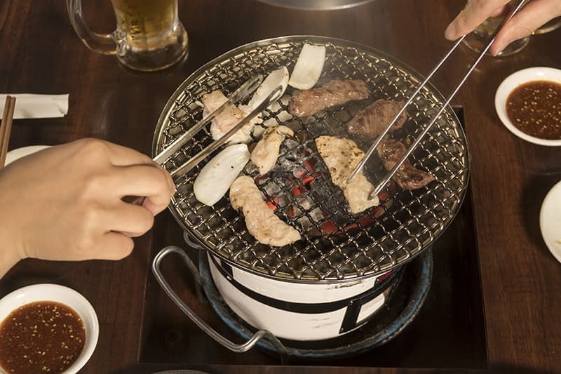 四条ホルモンで丸い七輪を囲み肉と玉ねぎを焼く様子