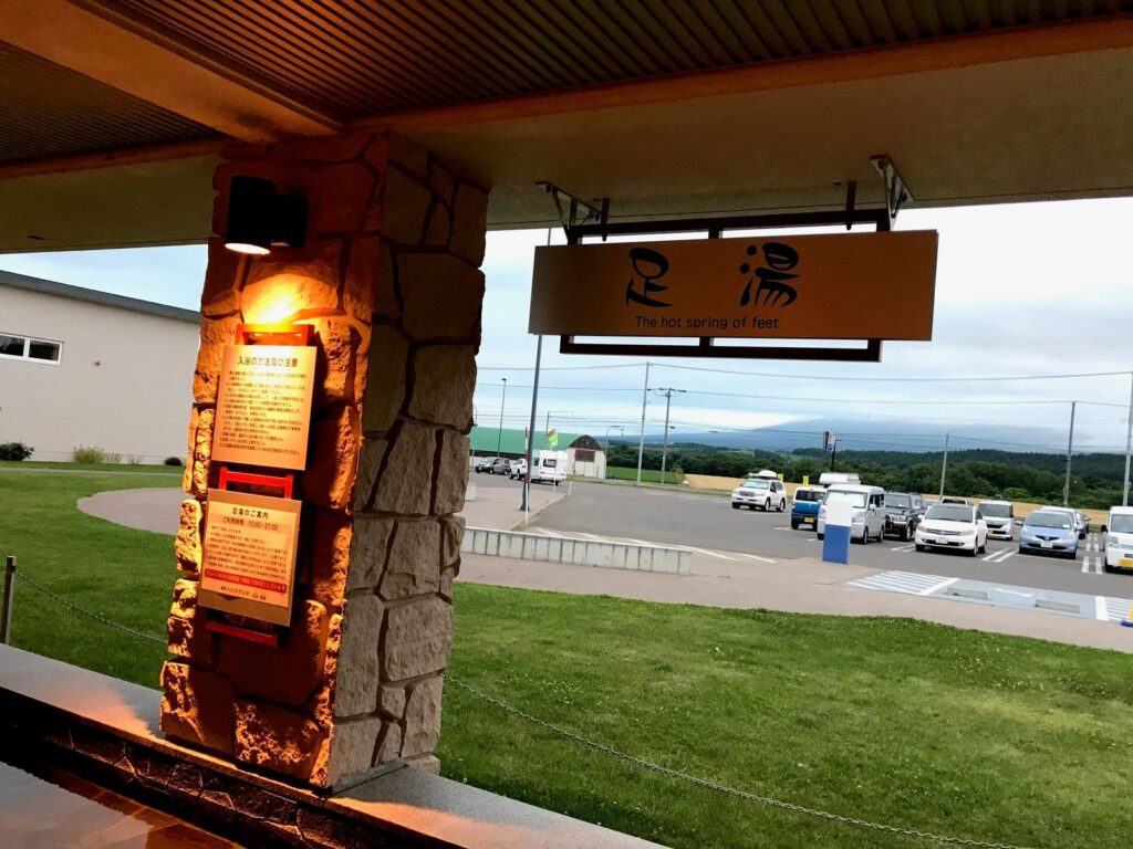 パパスランドさっつるの足湯の屋根と看板。奥には車でいっぱいの駐車場